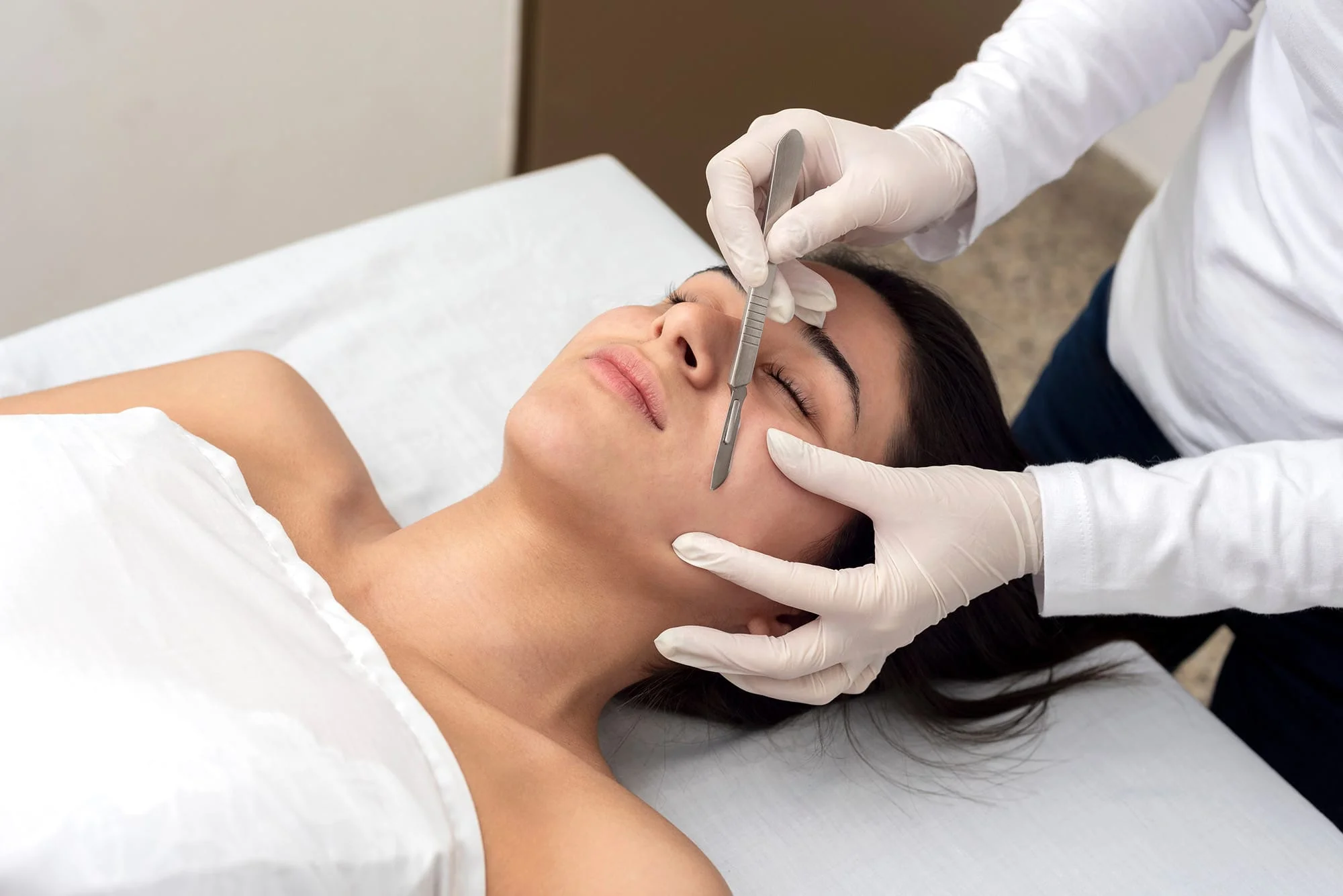 A practitioner performs dermaplaning with a facial blade.