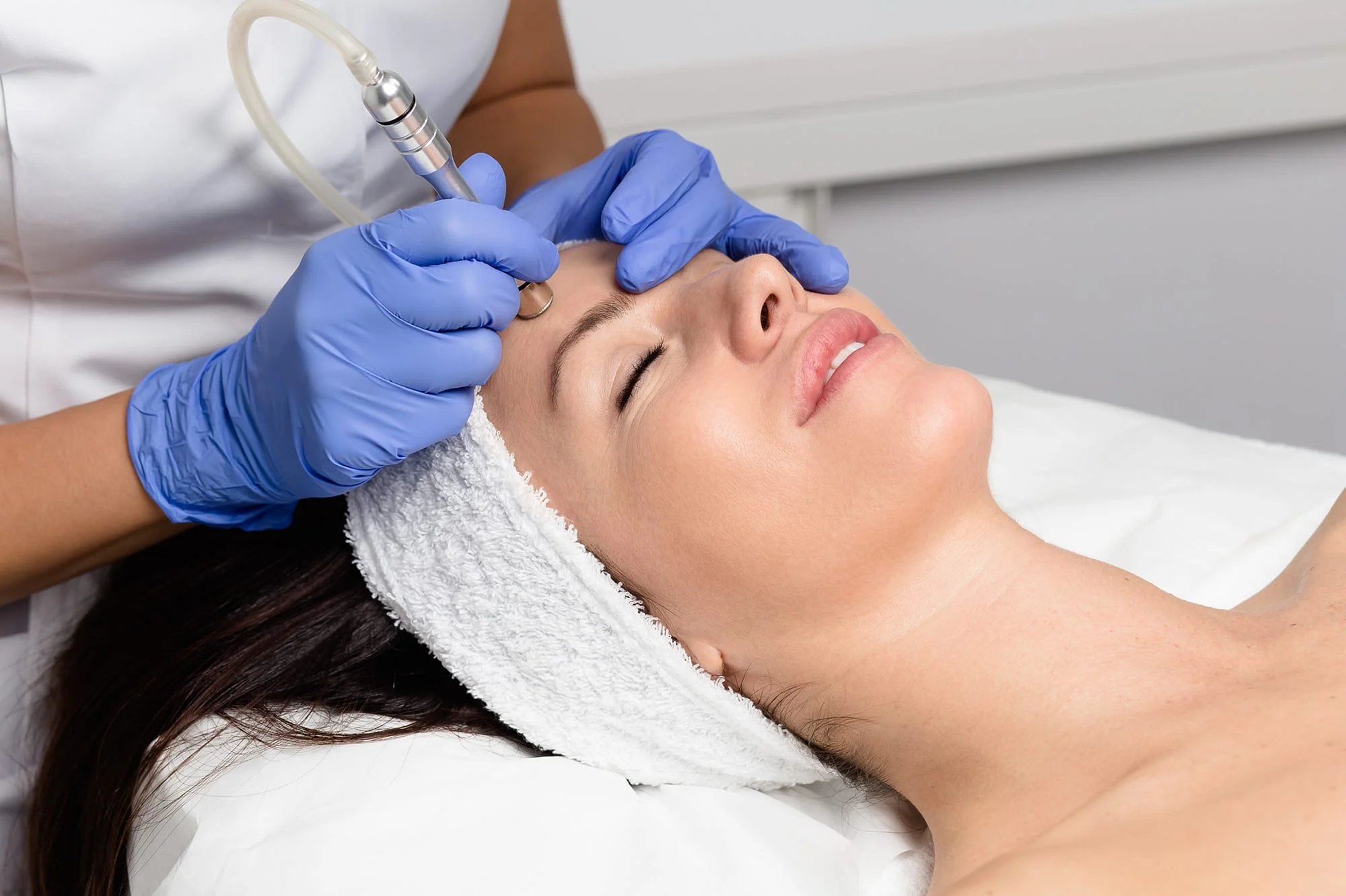 A practitioner uses a microdermabrasion handpiece on the face.